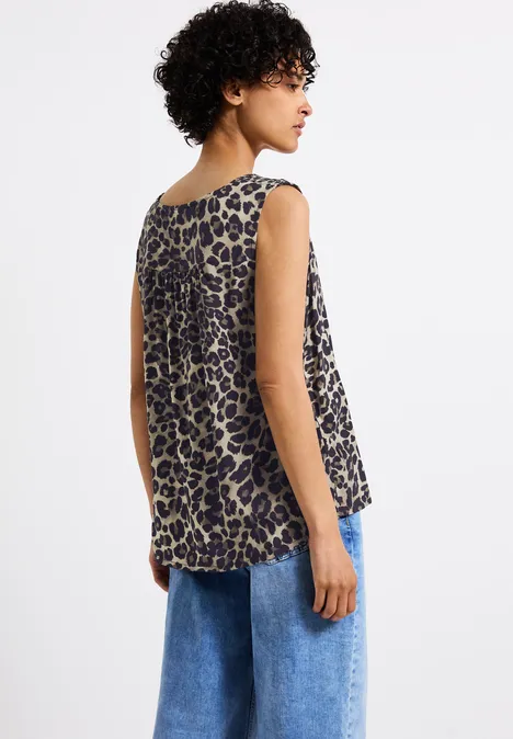 Frau mit lockigem Haar trägt ärmelloses Leoparden-Top und blaue Jeans, Rückansicht.